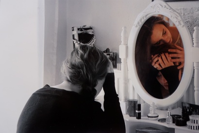 Ein Mädchen sitzt vor einem Spiegel, in diesem Sieht man eine jüngere Version des Mädchens.